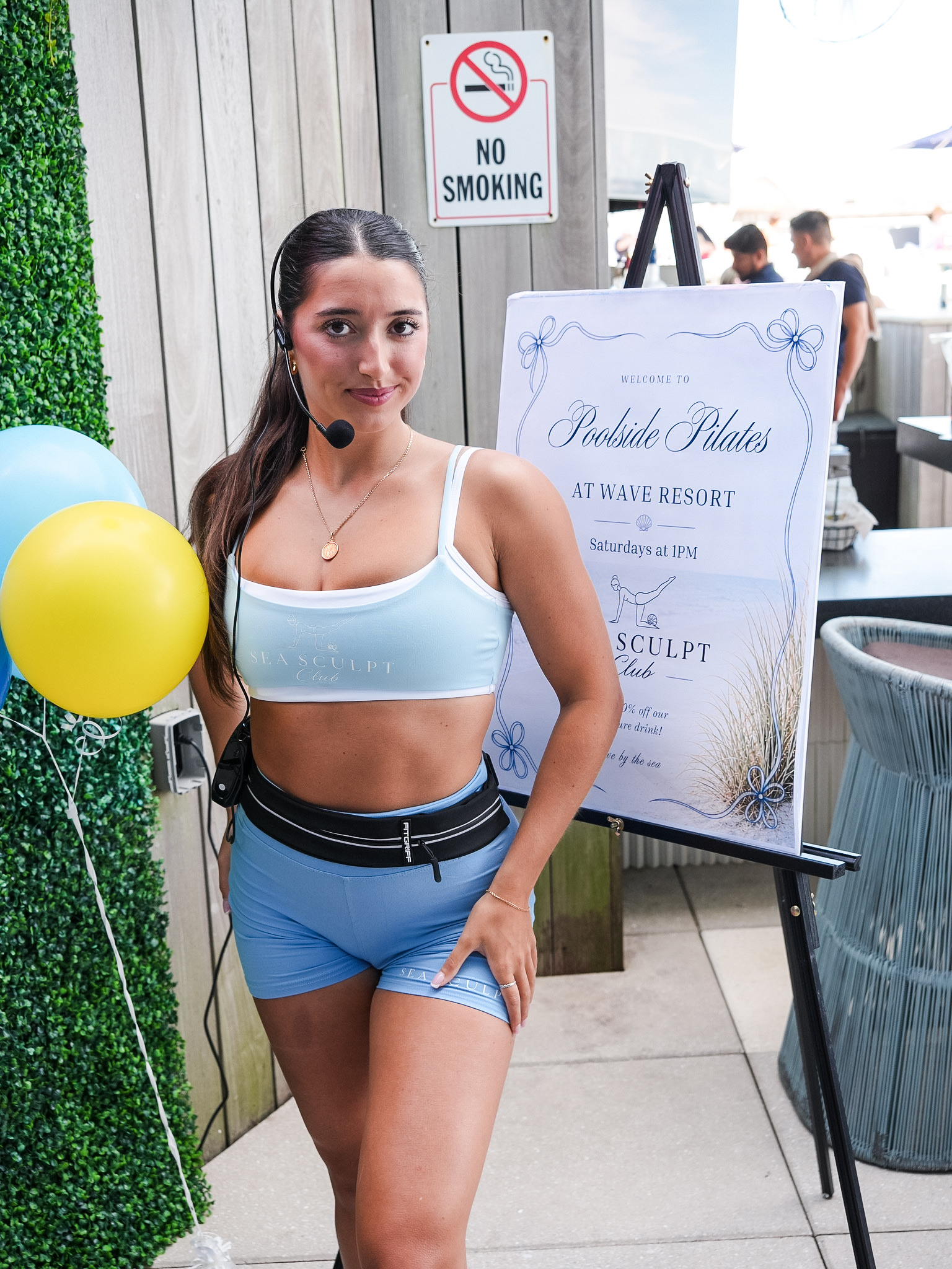 Sea Sculpt Club instructor beside the Poolside Pilates at Wave Resort welcome sign